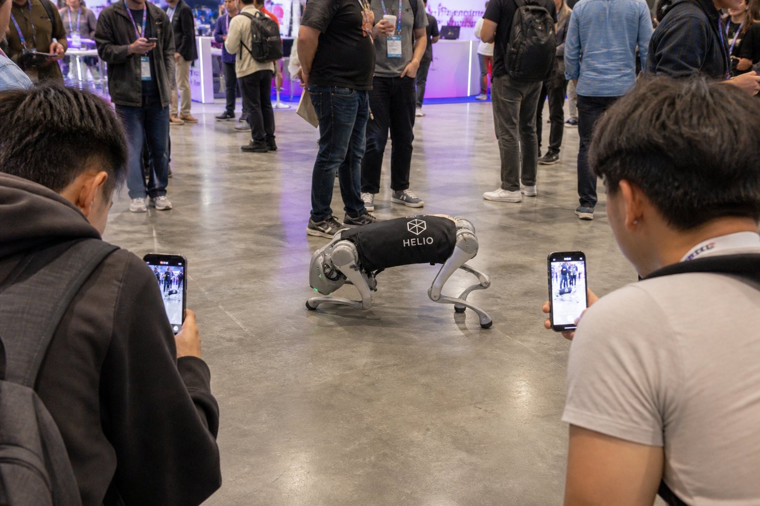 Attendees filming a robot dog in a black logo shirt.