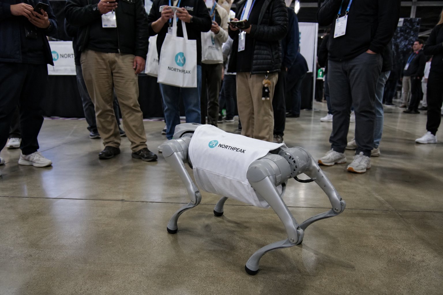 Robot dog in a white logo shirt with a crowd around a booth.