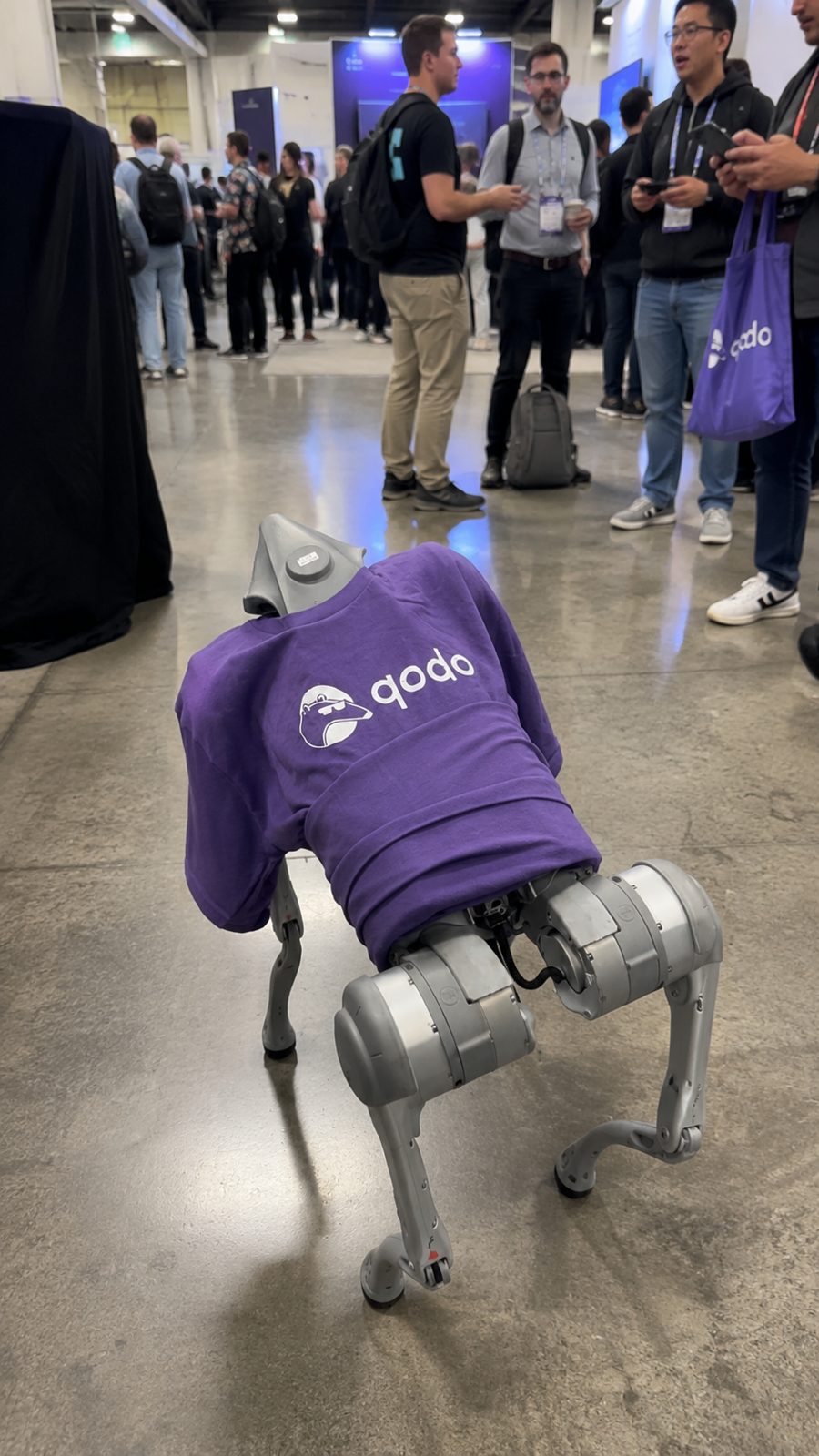 Robot dog in a purple Qodo shirt on the expo floor.